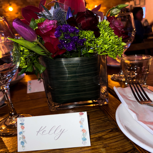 Floral arrangement in a vase on a table with a name card labeled 'Kelly'.